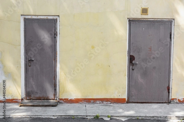 Fototapeta Part of the yellow stone wall of an old building and a closed rusty door