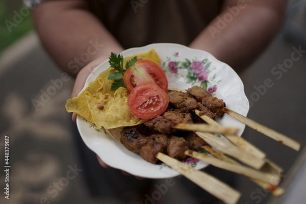 Fototapeta a serving of Balinese fish satay topped with fresh tomatoes, celery and crispy chips. Presented by hand by the waiter. Looks delicious and delicious appetizing