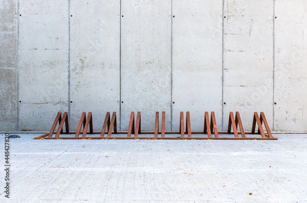 Fototapeta Row modern, empty bicycle racks, made of rusted metal or corten steel. Concrete wall in the background.