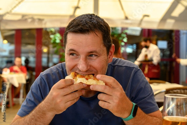 Obraz Mature man eating a slice of pizza in a restaurant. Medium shot
