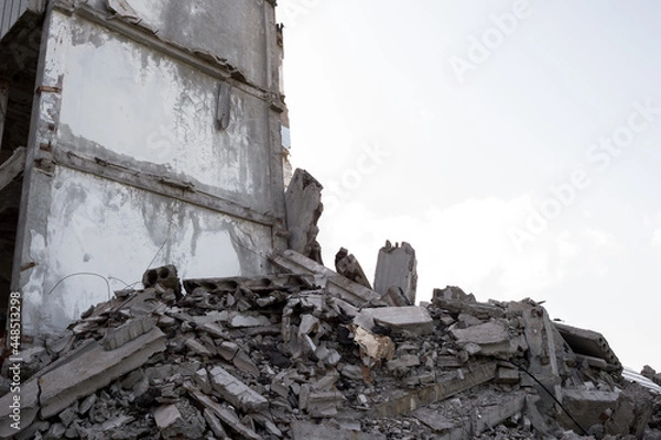 Fototapeta A pile of construction debris made of gray concrete fragments against the gray sky and the remains of a destroyed building. Background