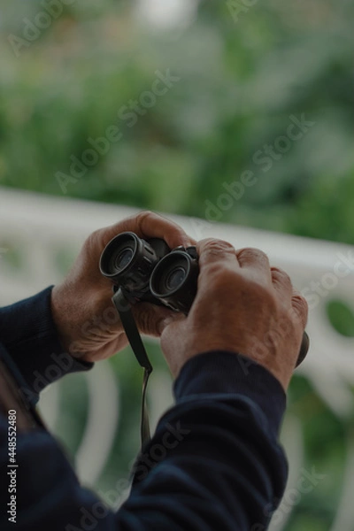 Fototapeta Hands of a man holding binoculars. Close-up image.