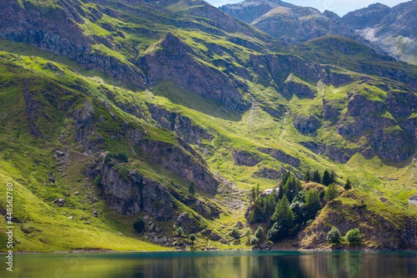 Obraz Mountain lake in the middle of the alps. Summer in the green mountain with a blue lake. Alpine mountains with a play of light and shadow of the clouds.