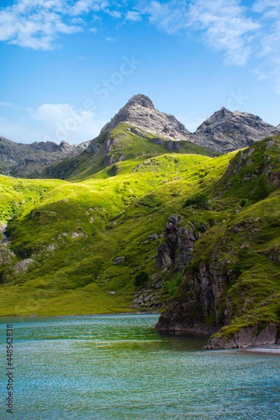 Obraz Mountain lake in the middle of the alps. Summer in the green mountain with a blue lake. Alpine mountains with a play of light and shadow of the clouds.