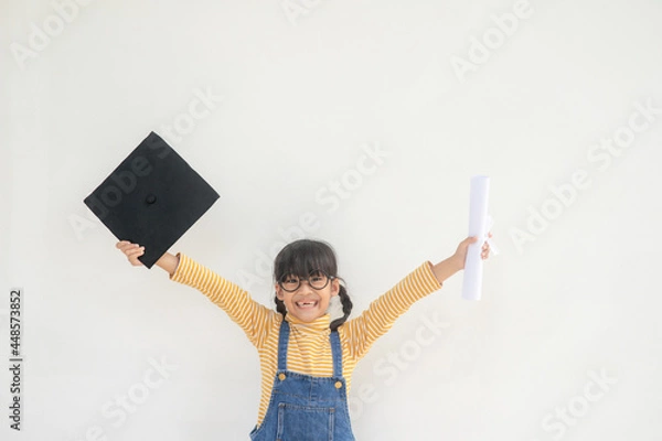 Fototapeta children girl wearing a graduate cap over white background very happy and excited doing winner gesture with arms raised, smiling and screaming for success. Celebration concept.