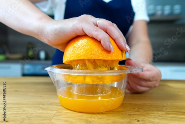 Fototapeta Hand squeezing orange juice. Close up fresh drink making process at home