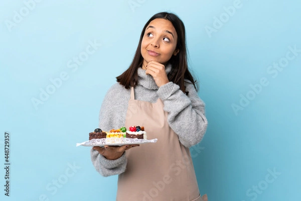 Fototapeta Pastry chef holding a big cake over isolated blue background thinking an idea while looking up.