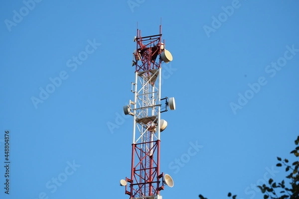 Fototapeta Telecommunications tower with a 5G cellular network antenna on a blue sky background.