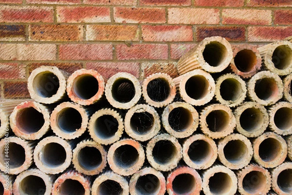 Obraz Terracotta clay brick pipes stacked against red brick wall with copy space