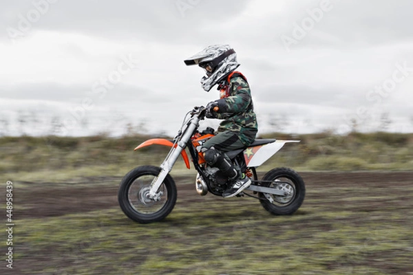 Fototapeta Child on his small motorcycle. Small biker dressed in a protective suit and helmet. The kid is engaged in motocross.
