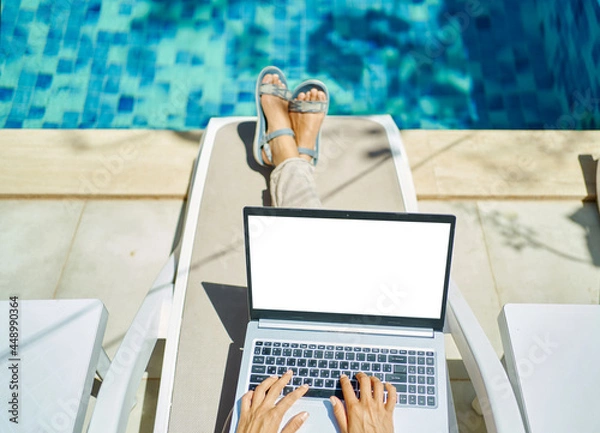 Fototapeta top view woman working on laptop computer with white blank screen, female hands typing keyboarding text, lying by the pool