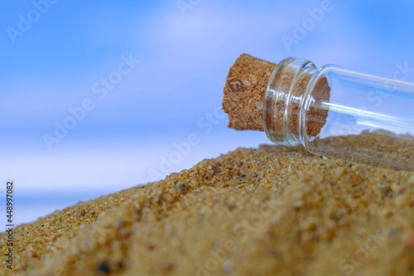 Fototapeta small glass jar with a cork lying on the sand