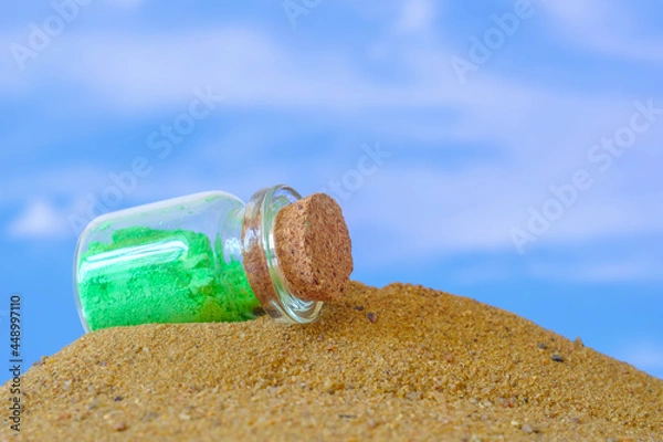 Fototapeta small glass jar with a cork lying on the sand