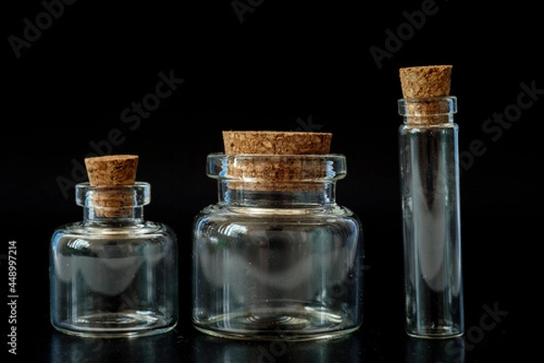 Fototapeta small glass jars with a cork on a black background