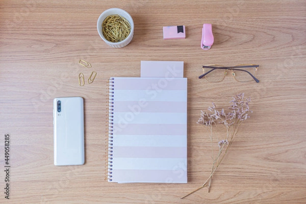 Fototapeta Workspace with pale pink and white stationary on wooden background. Flat lay, top view. Feminine desk concept.