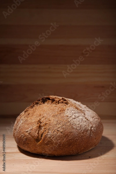 Obraz Handmade fresh wheat bread on wooden background in the contrast light. vertical frame side view with space area for text or design