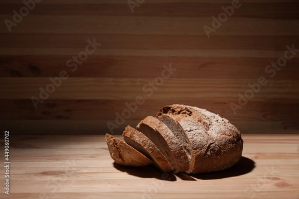 Obraz Fresh handmade wheat bread cut into pieces on wooden background in the contrast light. horizontal frame side view with space area for text or design
