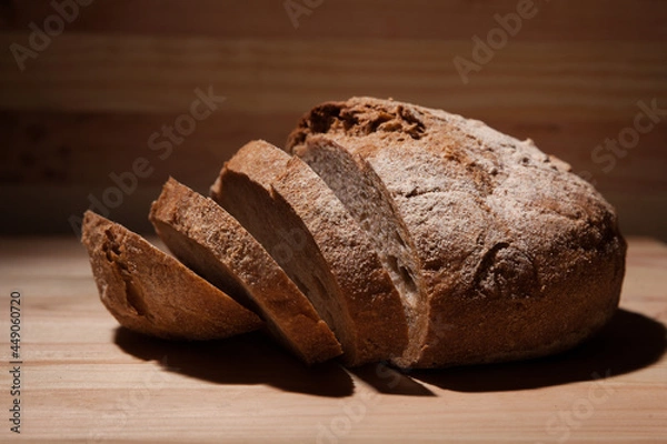 Obraz Fresh handmade wheat bread cut into pieces on wooden background in the contrast light. horizontal close-up frame side view