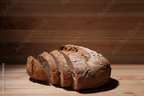 Obraz Fresh handmade wheat bread cut into pieces on wooden background in the contrast light. horizontal frame side view with space area for text or design