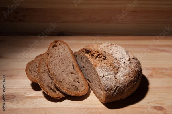Obraz Fresh handmade wheat bread cut into pieces on wooden background in the contrast light. horizontal frame high angle view