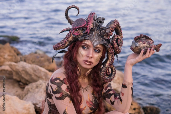 Obraz beautiful girl in the costume of the sea witch Ursula, holding a fish in her hand, against the background of the sea, close-up, portrait