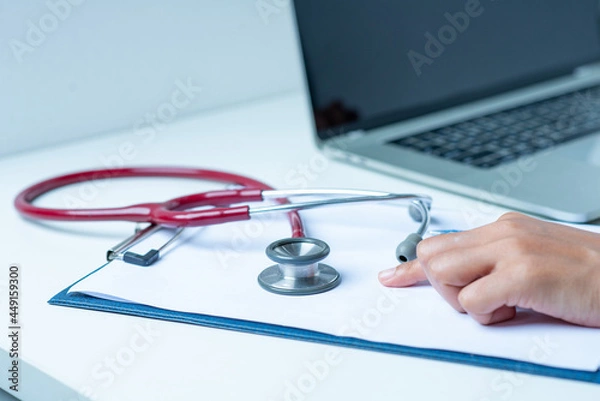 Fototapeta the doctor is analyzing the illness A stethoscope and computer are placed on a white desk in a white background.