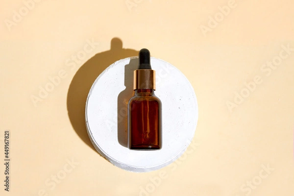 Fototapeta Cosmetics bottle with dropper staying on the pastel beige background. 
Earth colors, zero waste containers. Mockup concept. Minimal boxes and geometric podium. Scene with geometrical forms. 
