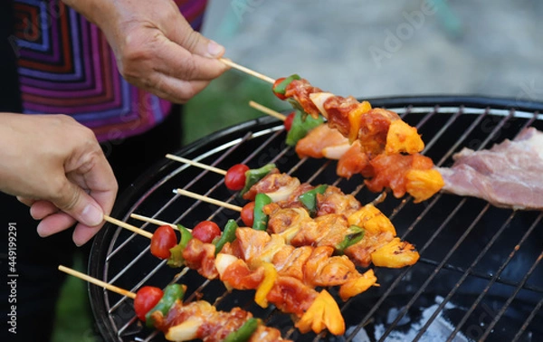 Fototapeta Closeup of  fresh raw  chicken barbecue on gridiron with woman's hands. 