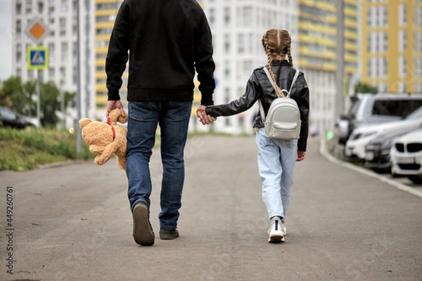 Fototapeta Pedophile man holds the hand of teenage girl in street. The concept of kidnapping and child trafficking. Rear view on pedophile with toy and caucasian child girl walking along the street. Crime