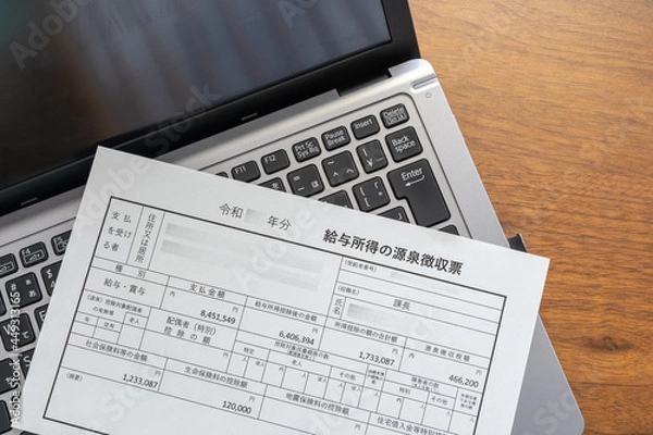 Obraz パソコンに置かれた会社で働くサラリーマンが受け取る給与・賞与所得の源泉徴収票　支払金額、給与所得控除後、所得控除後の額、源泉徴収税額等