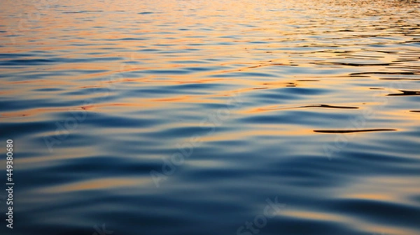 Fototapeta Reflection of sunset in waves of river, selective focus. Water surface with waves in the evening. Ripple water texture.