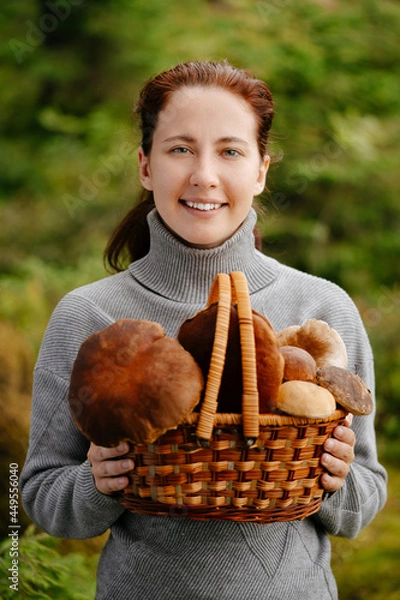 Fototapeta A happy woman with a basket of mushrooms in the forest. Portrait of a forester with a harvest.