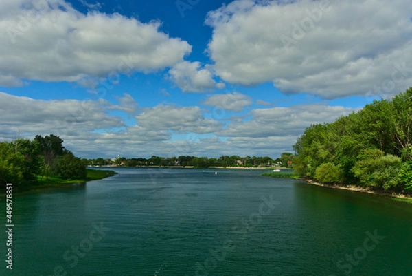 Fototapeta Islands of Boucherville national park in Lawrence (Laurent) River, Montreal, QC on a cloudy summer day. The trees and grass on the river banks. A boat on the river