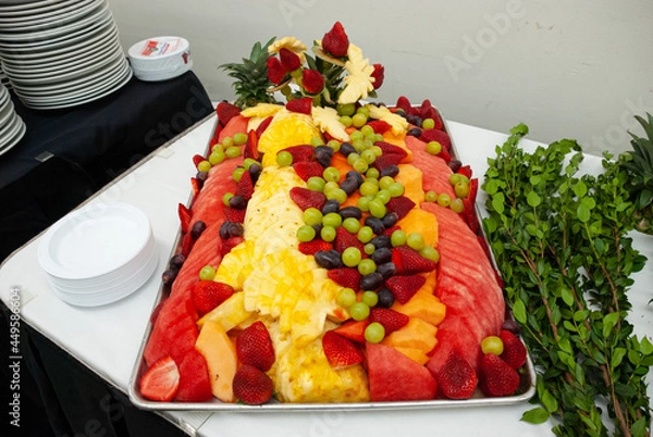 Fototapeta Tray filled with fresh fruit setup on a white table with greenery on the side.