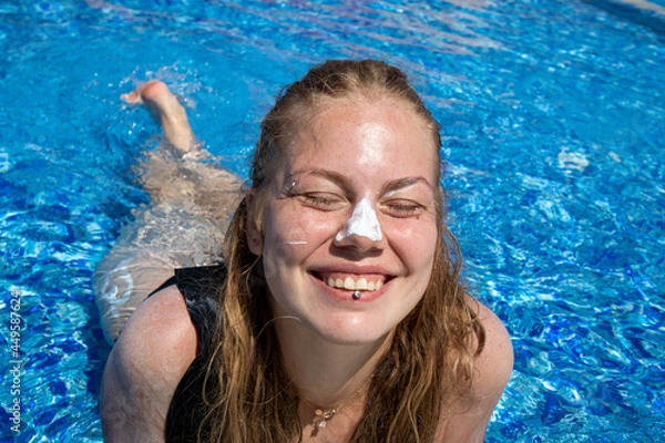 Fototapeta girl with sunscreen on her nose swims in the pool close-up