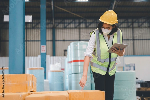 Fototapeta Factory woman staff in medical face mask and protective safety using digital tablet working checking inventory storage at textile warehouse