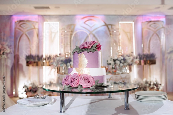 Obraz The wedding cake. White, two-tiered, decorated with flowers and gold. On a delicate pink background. Side view, top.
