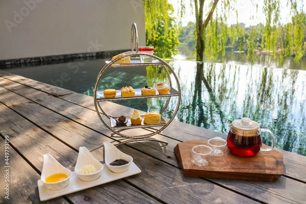Obraz Afternoon tea set with dessert on wooden floor beside swimming pool