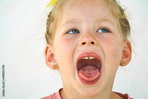 Obraz Cheerful child. Girl laughs close-up of the face on a white background. A little girl show tongue throat. portrait with wide open mouth and protruding tongue. with clear view pulls out long tongue
