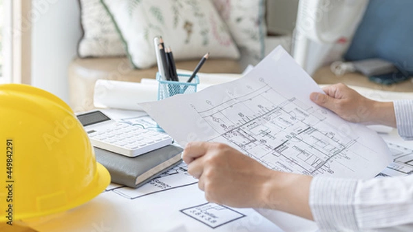 Fototapeta Architectural building design and construction plans with blueprints, Young man was designing a building or architecture with a ruler, pen, pencil, tape measure, architect hat and other equipment.