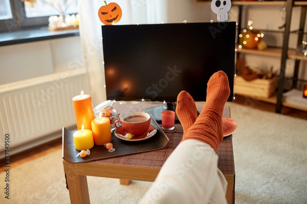 Fototapeta halloween, holidays and leisure concept - young woman watching tv and resting her feet on table at cozy home