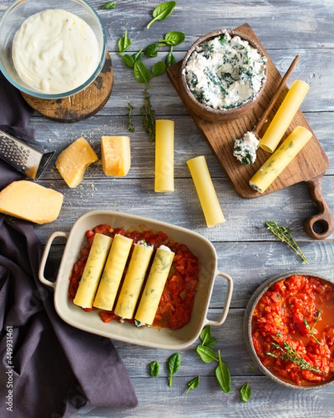 Obraz Italian cuisine. Cannelloni with spinach and ricotta. Cannelloni is prepared with parmesan cheese in tomato sauce. Italian dinner. Italian food on a gray wooden background. Bechamel sauce