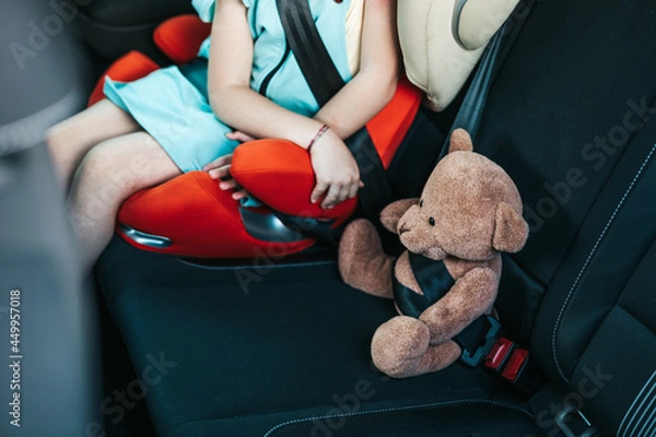Fototapeta Little girl sitting in a car on a safety child car seat with her teddy bear.