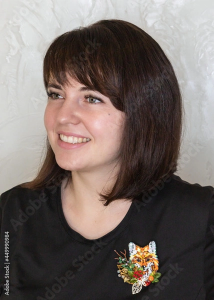 Obraz Portrait of a young woman with a handmade brooch on a light background. Facial expression, selective focus, beautiful people.