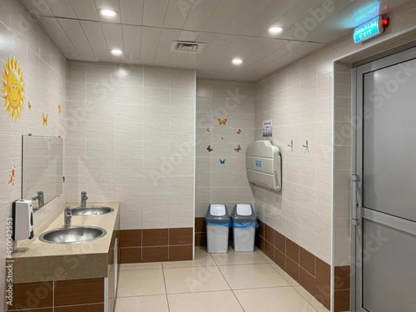Fototapeta Public toilet for children. A washbasin, drawings on the walls, a changing table for babies. The door with the Russian inscription - Exit