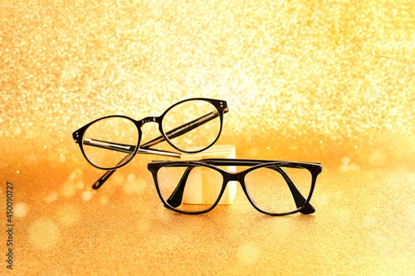 Obraz A pair of  black eyeglasses on golden glitter background
