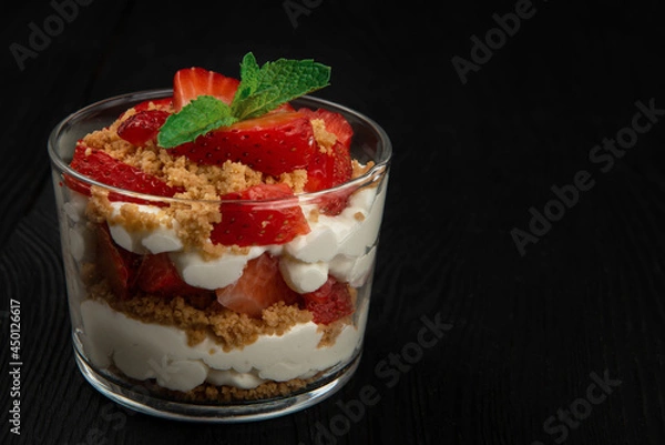 Fototapeta Strawberry with cookie and cream dessert decorated with mint leaf on black wooden background, with copyspace