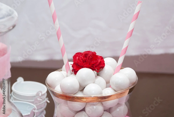 Fototapeta big white gumballs in a crystal container with a red flower on top and two pink and white paper straws