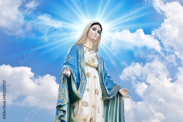 Fototapeta Statue of Our lady of grace virgin Mary with Bright Blue Sky and beautiful clouds with abstract colored background and wallpaper at Thailand.