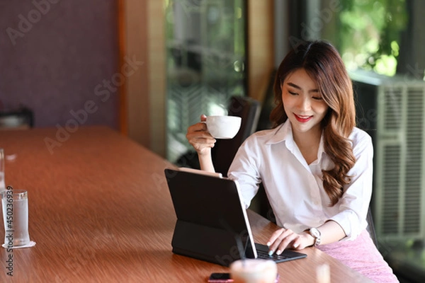Fototapeta Beautiful businesswoman drinking coffee and checking email with computer tablet.